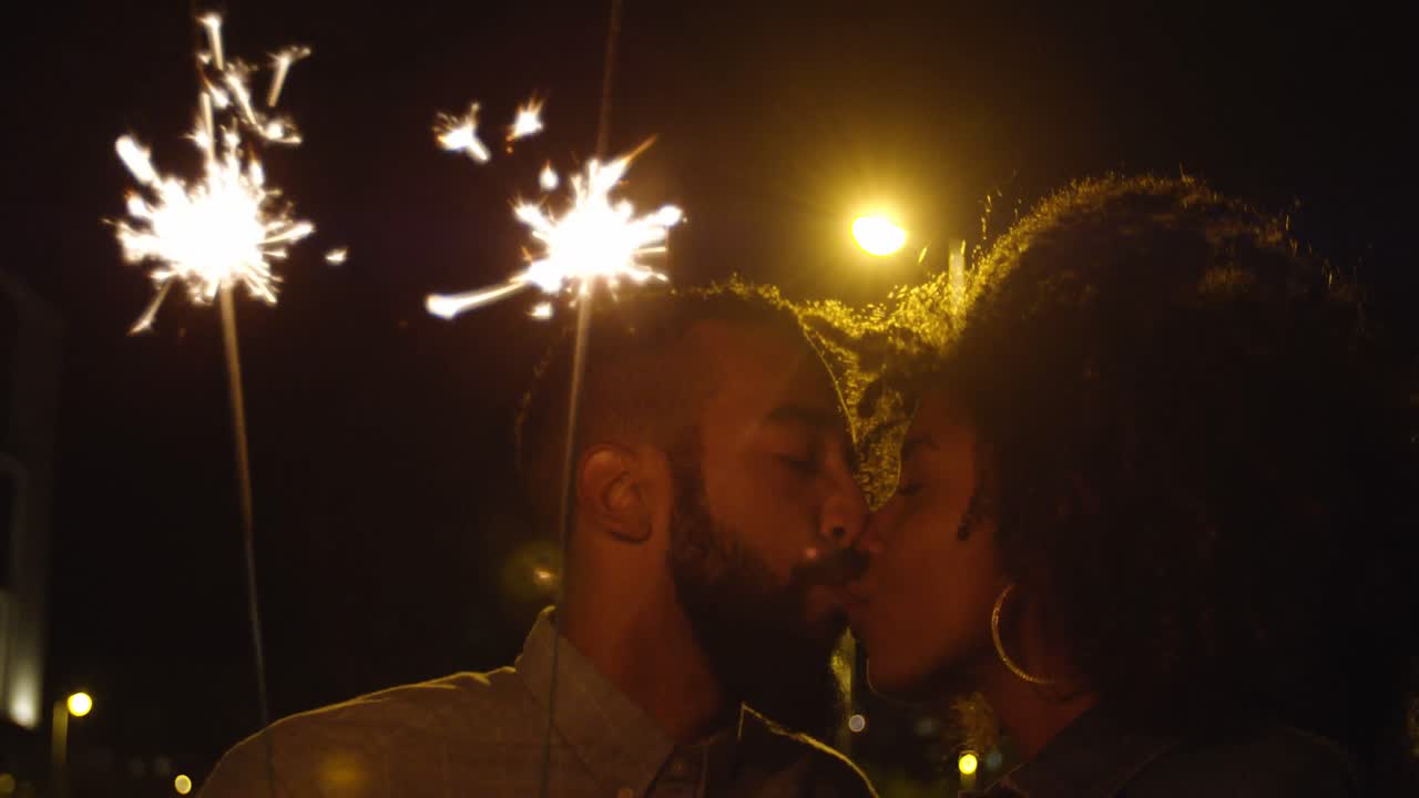 Pareja besándose mientras sostiene bengalas en la ciudad 4k