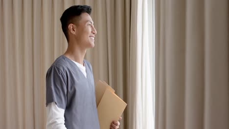 Portrait-of-happy-biracial-male-doctor-against-beige-curtains-with-copy-space,-slow-motion