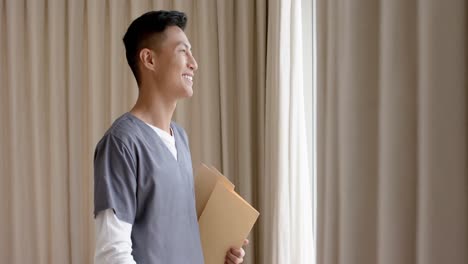 portrait of happy biracial male doctor against beige curtains with copy space, slow motion