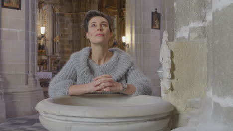 woman prays by holy water font and makes cross shape with hand cu