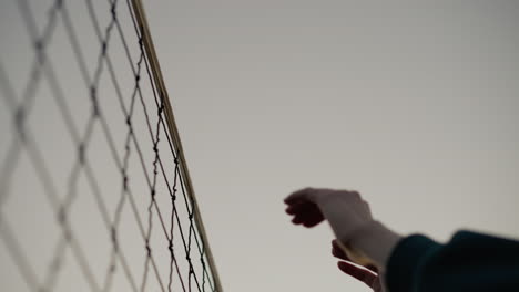 upward hand view of volleyball players reaching to hit ball over net, capturing dynamic moment of play with volleyball net in focus, outdoor court and sky background