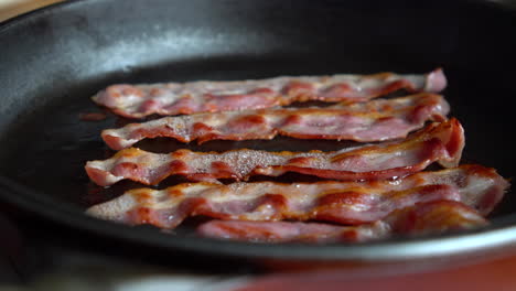 Crispy-bacon,-rich-in-fat-and-colour,-sizzling-and-smoking-in-a-hot-pan