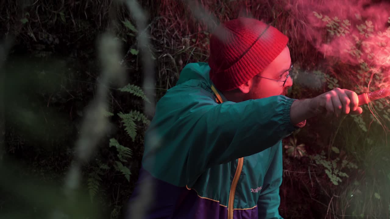 Man holding a red flare in the forest at night