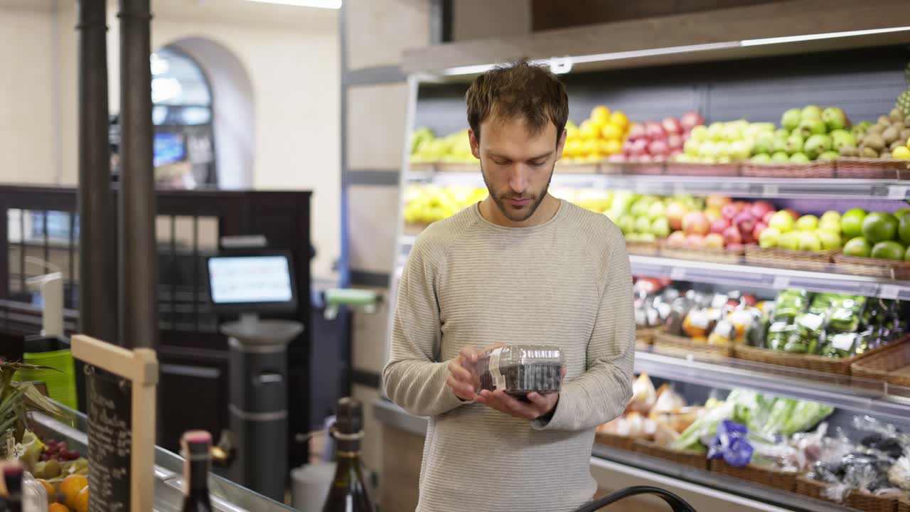 el hombre toma unas bayas frescas del estante de alimentos. el comprador elige arándanos en la tienda de comestibles.