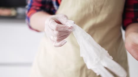 Woman-putting-on-culinary-gloves-on-kitchen,-close-up