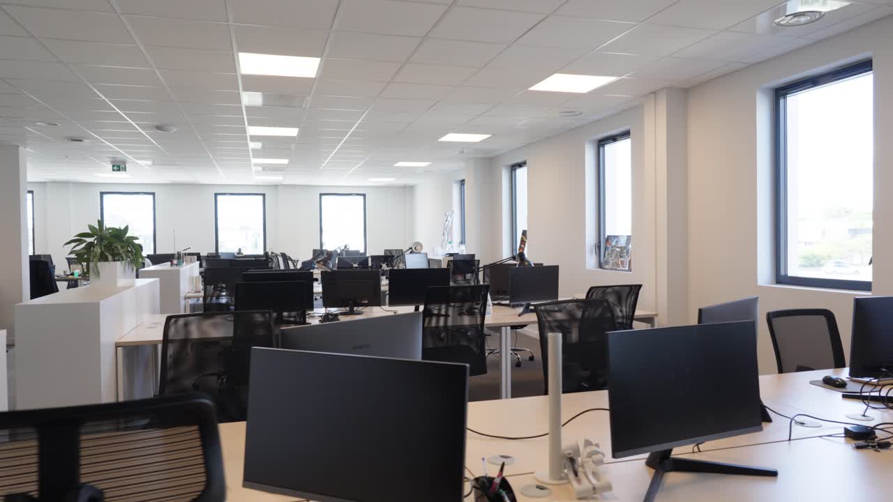 Slow establishing shot of an empty office with laptop screens on desks