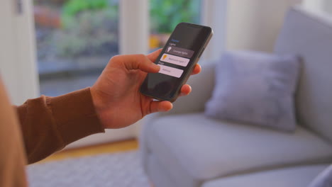 close up of man at home looking at app on smart phone to control lights
