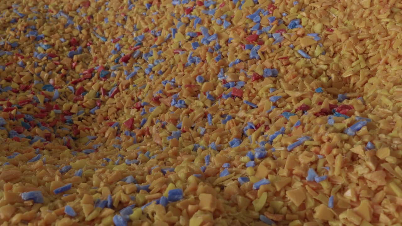 Mucchio di scaglie di plastica triturata multicolore (materiale arancione, blu e rosso) in una fabbrica di riciclaggio.