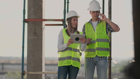 The-controller-is-a-man-of-a-building-under-construction-talking-on-the-phone-with-management-and-has-discussed-with-the-engineer-and-architect-woman-construction-progress.