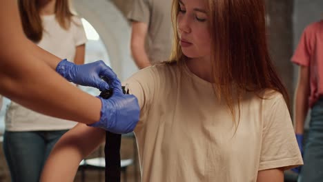 Primer-Plano:-Una-Niña-Aprieta-Un-Torniquete-Médico-Y-Lo-Fija-En-El-Hombro-De-Otra-Niña-Durante-Un-Curso-Práctico-De-Medicina.-Entrenamiento-De-Primeros-Auxilios.