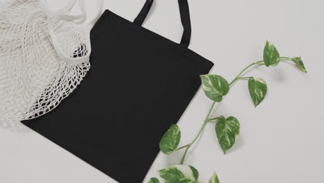 Close-up-of-white-and-black-bags-with-green-plant-on-white-background,-with-copy-space,-slow-motion