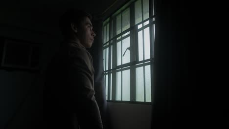 side portrait of man in room opening curtains and looking out through window in morning. medium shot
