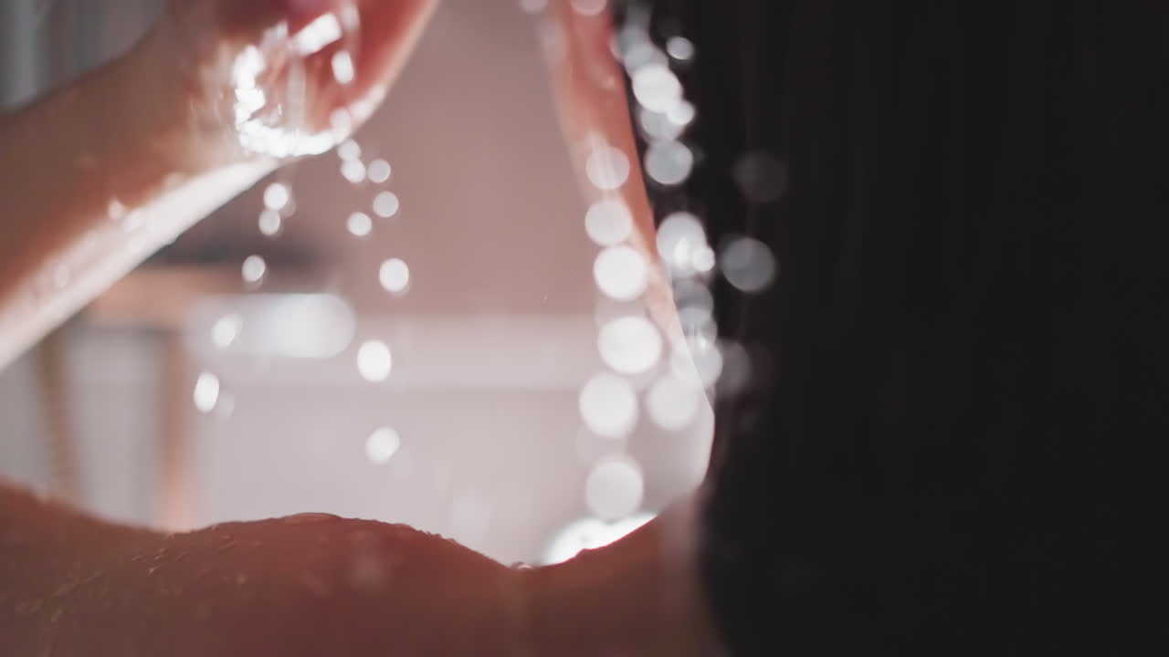 la señora toma cuidadosamente una ducha calmante lavando el cabello. el agua caliente cae en cascada por la piel de la mujer. la joven toma una ducha limpiando la piel con agua caliente