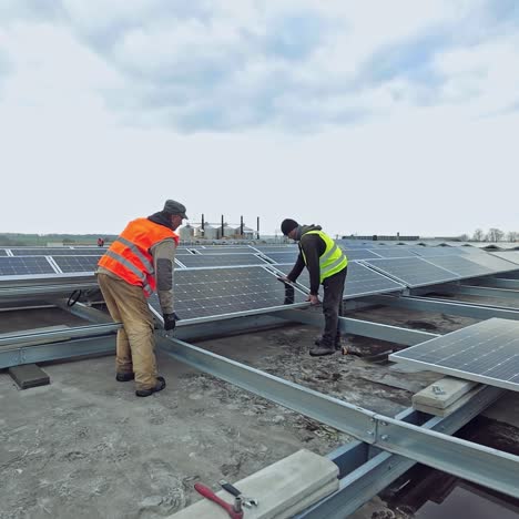 technicians installing solar panel on metal base. two workers laying down and installing solar panels on flat roof. pv panel converts solar energy into electric energy.