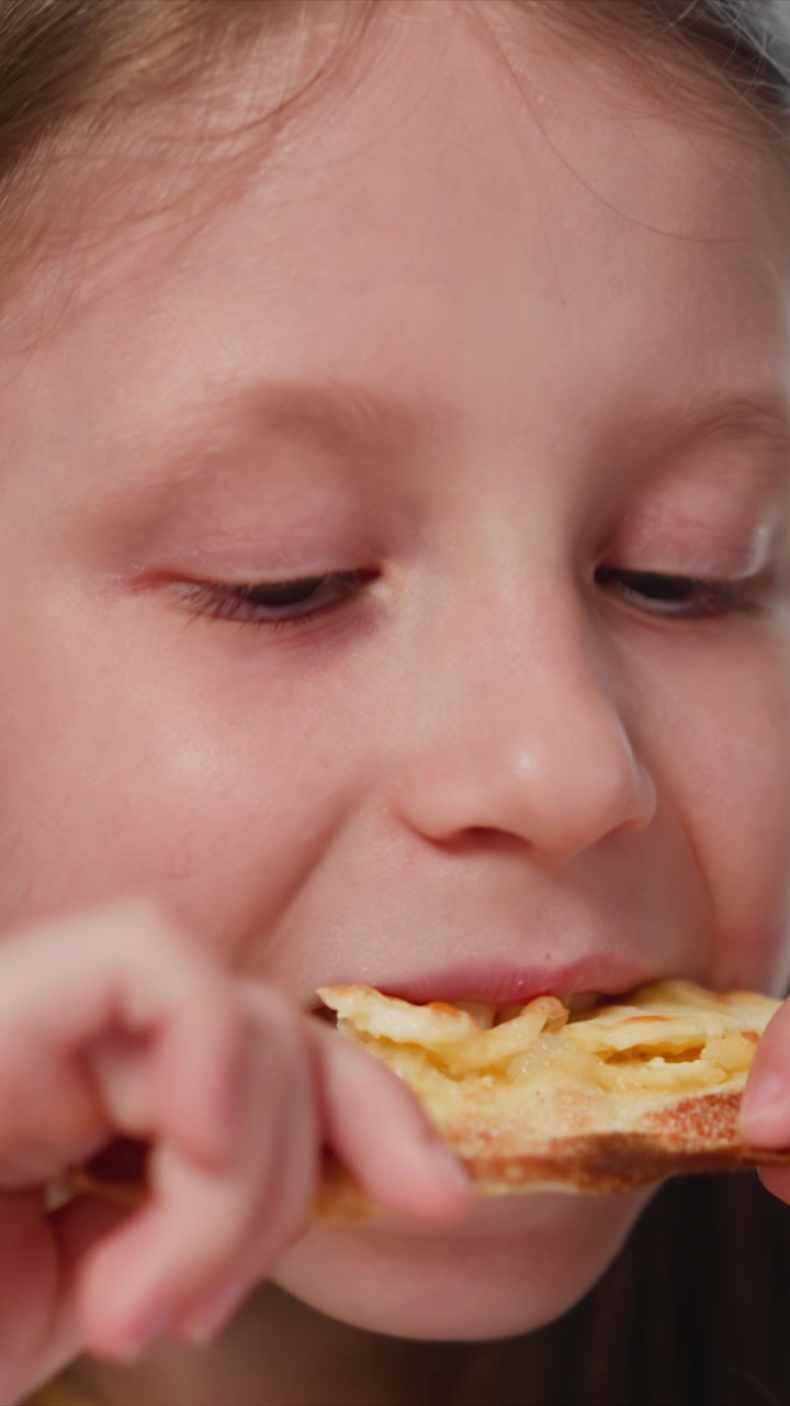Close up of young girl eating pizza. sequence shows child holding and taking bites from thin crust cheese pizza with soft lighting highlighting her facial features and hands. Background
