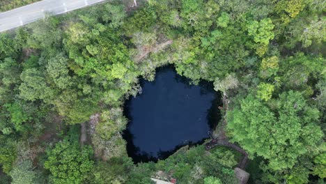 Aerial-ascends-from-natural-Cenote-Kikil-revealing-narrow-jungle-road