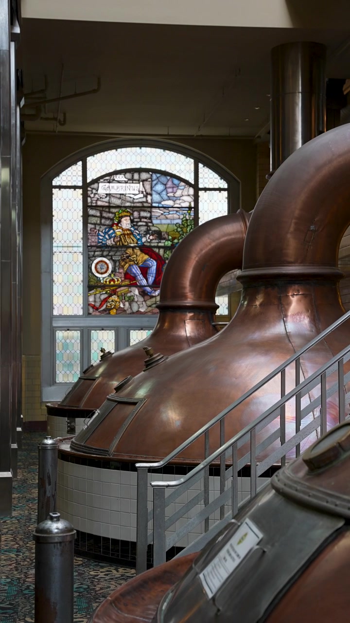 Gleaming copper brewing vats positioned in front of a vibrant colorful stained glass window in a historic brewery.