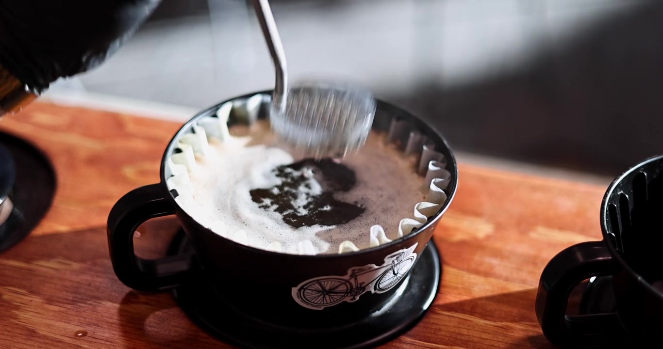 Barista rører blomstrende kaffe under pour-over-ekstraktion med en dispersionsskærm og kedel, ryster vand for at presse hver sidste dråbe ud, slowmotion