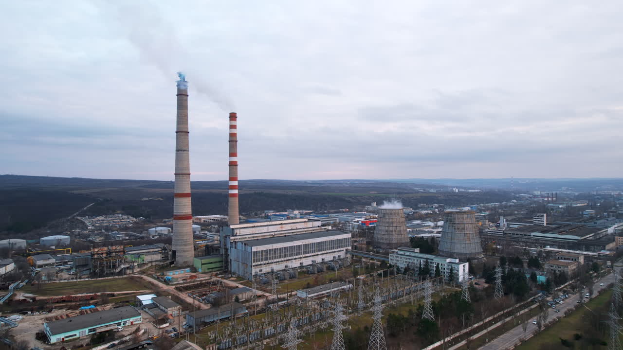 Aerial drone view of thermal power plant in Chisinau at cloudy weather, Moldova. View of pipes with felling steam, buildings and bare trees around