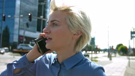 young beautiful woman with blonde hair and green eyes wearing a blue button up top in city on phone anxiously receiving bad news and having a conversation