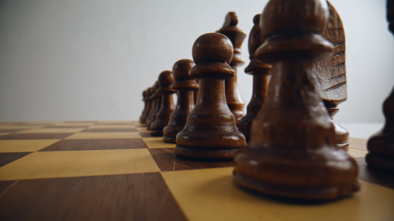 Brown wooden chess pieces positioned on board closeup. Dark figures standing
