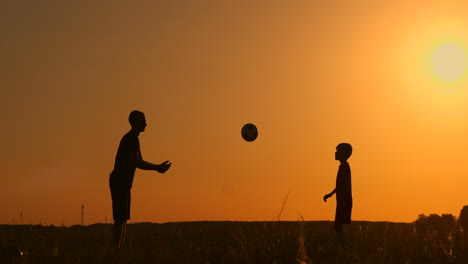 father and son playing football in the park at sunset silhouettes against the backdrop of a bright sun slow-motion shooting.