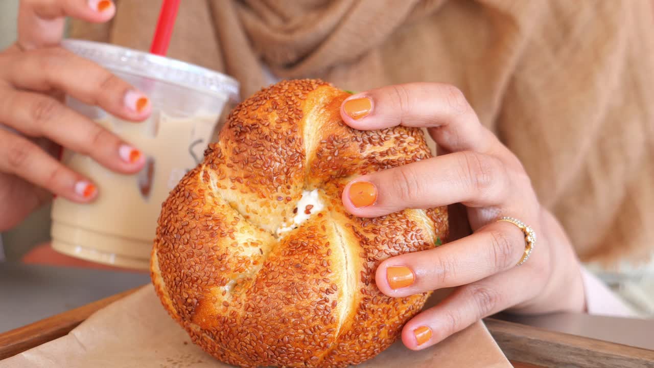 Woman Eating a Sesame Bagel and Drinking Iced Coffee