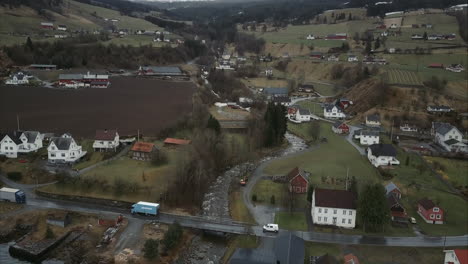 Toma-Aérea-De-Autos-Pasando-Un-Pequeño-Puente-Sobre-Un-Arroyo-En-El-Pueblo-De-Utvik,-Noruega