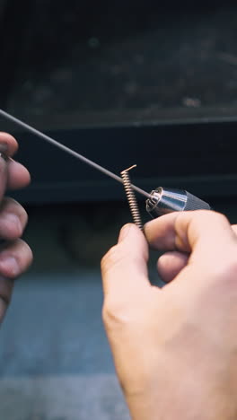 cu: jeweler coils thin gold wire turning handle of special tool at equipped workplace in craft workshop close view