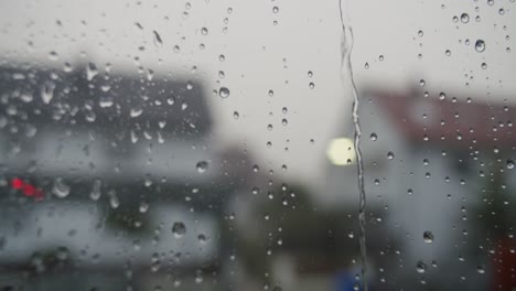 Close-up-of-raindrops-hitting-a-window-during-a-thunderstorm,-lightning-during-the-shot