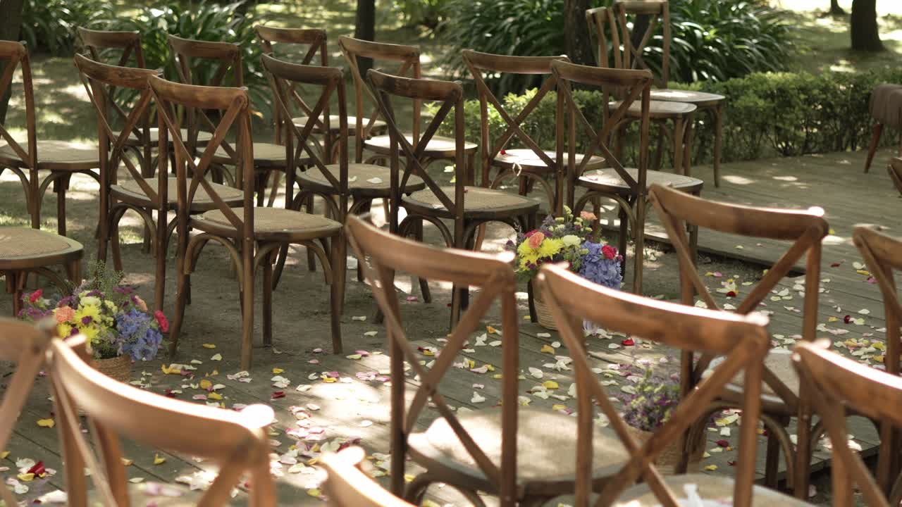 Wooden chairs arranged for an outdoor wedding ceremony with scattered flower petals