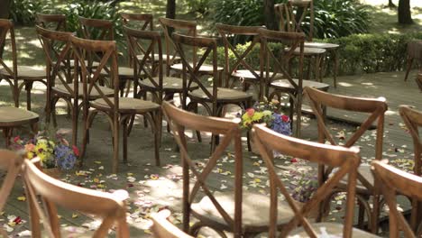 wooden chairs arranged for an outdoor wedding ceremony with scattered flower petals
