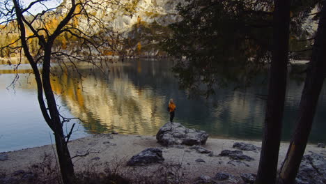 On-the-shores-of-Lake-Braies-in-Italy,-a-woman-with-blonde-hair-stands-on-a-rock