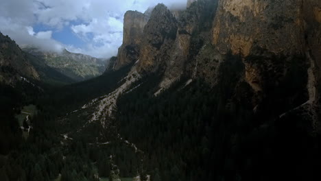 steady aerial shot with swirling clouds above a dark, imposing and rugged valley with high cliffs and dark forests