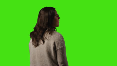 rear view of young woman standing waiting and looking around against green screen background