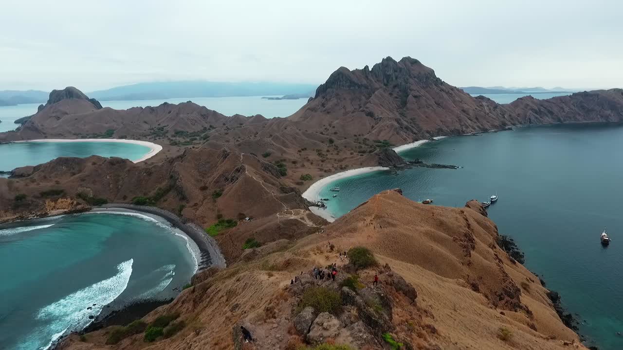vista aérea de la gente haciendo senderismo en la isla de padar, en el parque nacional de komodo, día nublado, en indonesia - inclinación hacia abajo, disparo de drones
