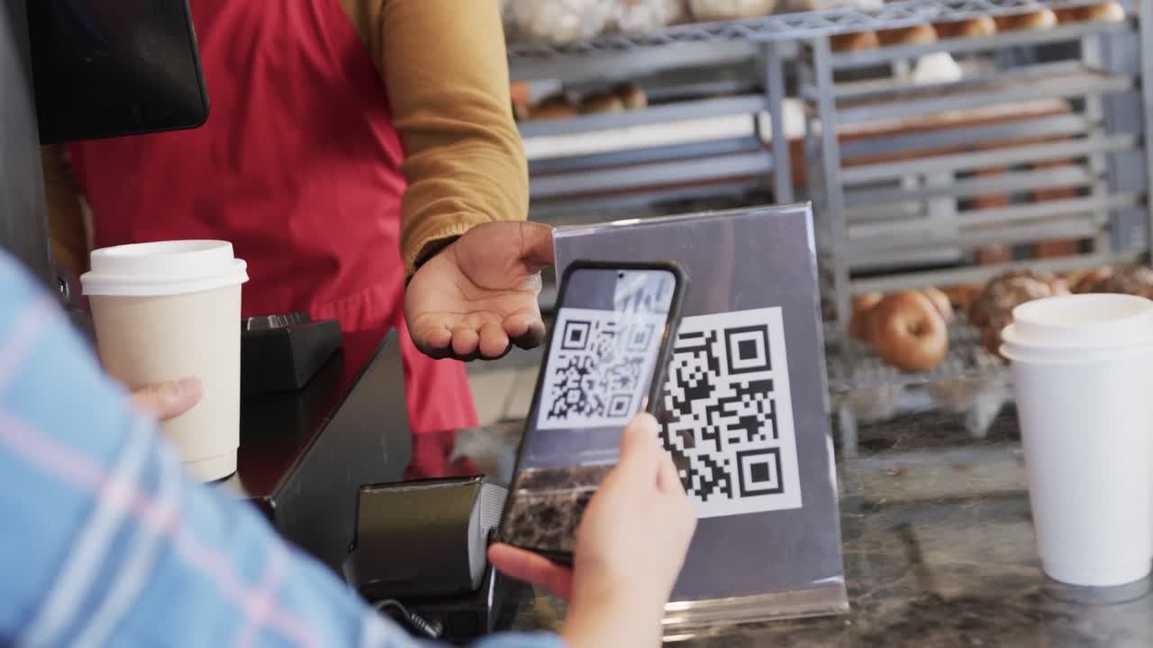 Diverse worker and customer scanning qr code with smartphone in bakery in slow motion