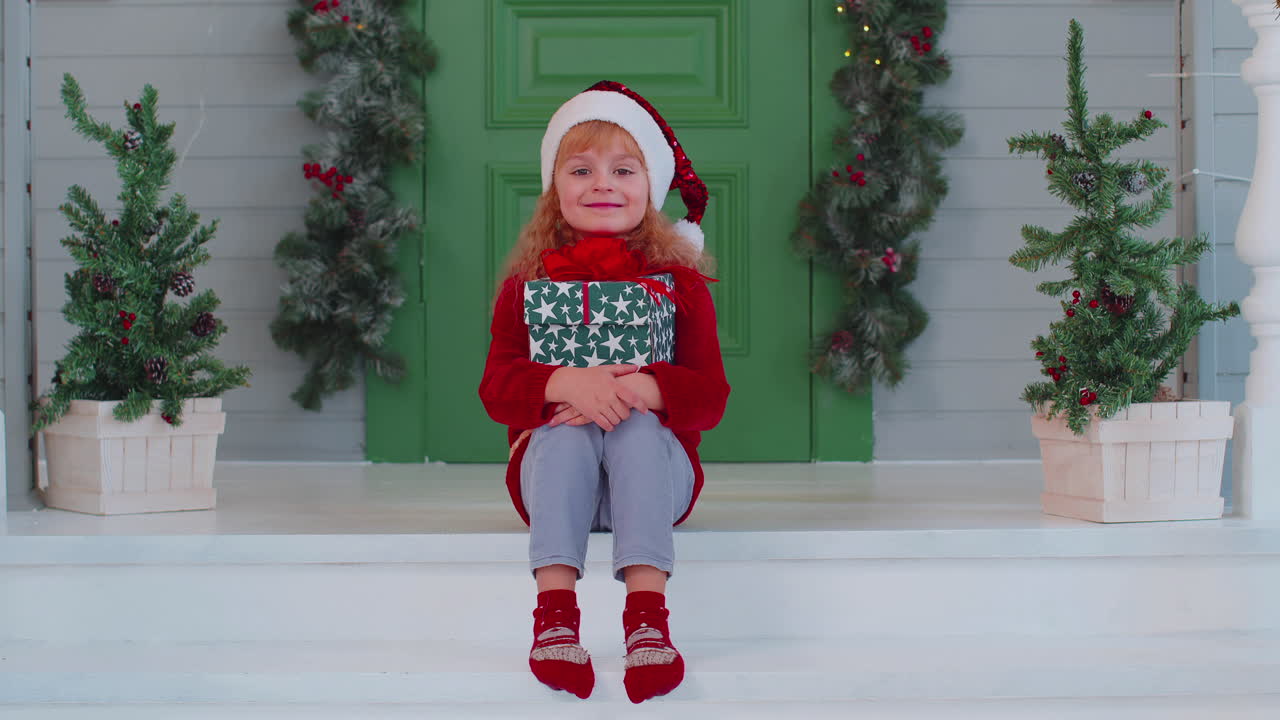 alegre niño sonriente niño niña niño sentado en el porche de la casa decorada sosteniendo una caja de navidad