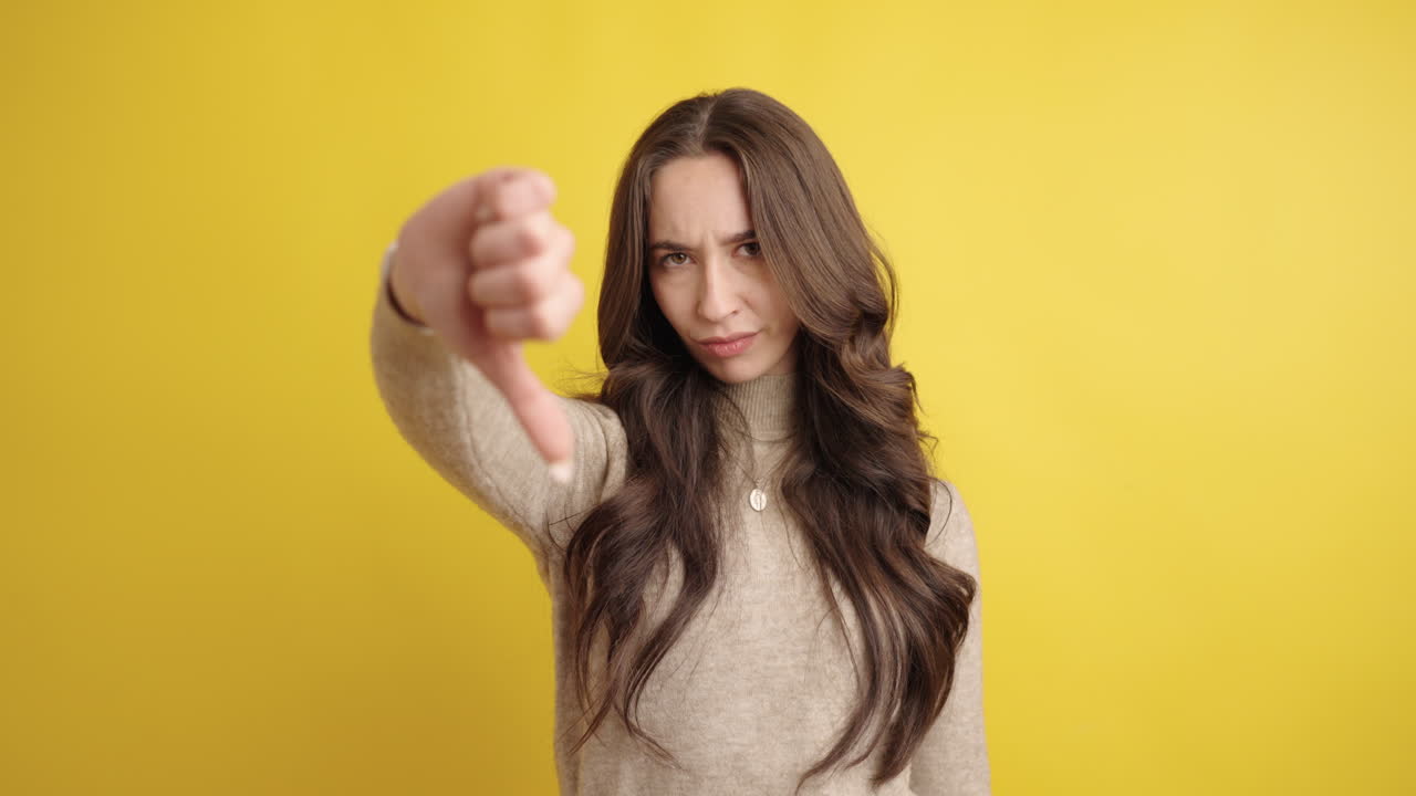 Young woman showing thumbs down on yellow background