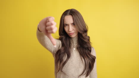 young woman showing thumbs down on yellow background