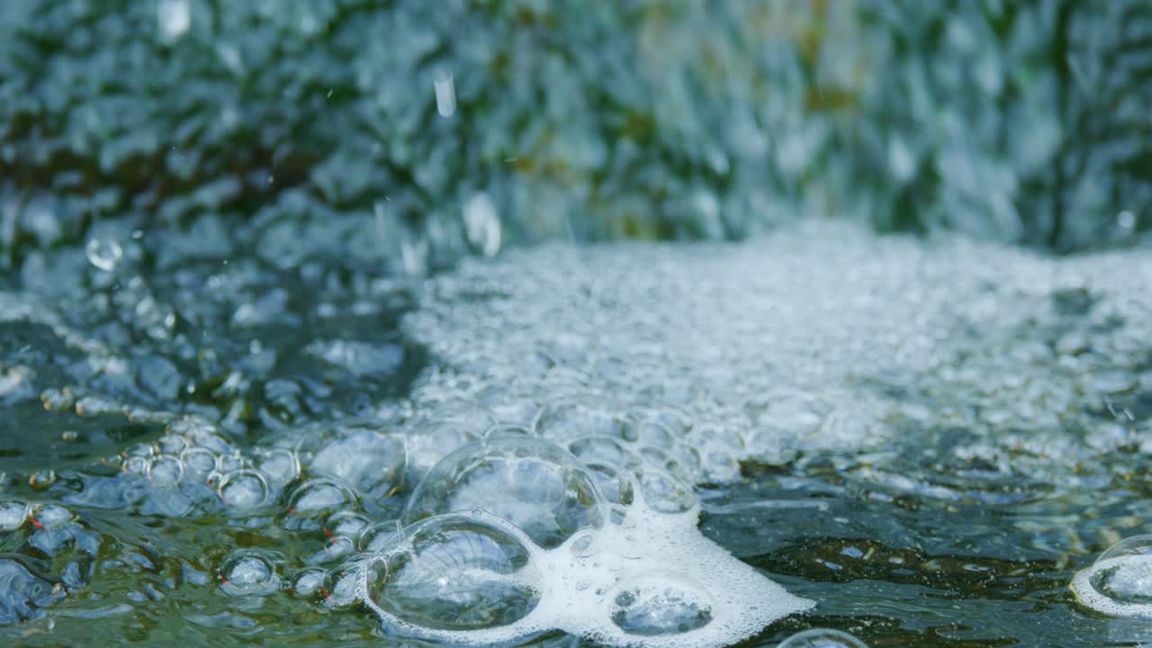 Close-up of bubbling pond water, koi and goldfish visible beneath surface, natural daylight