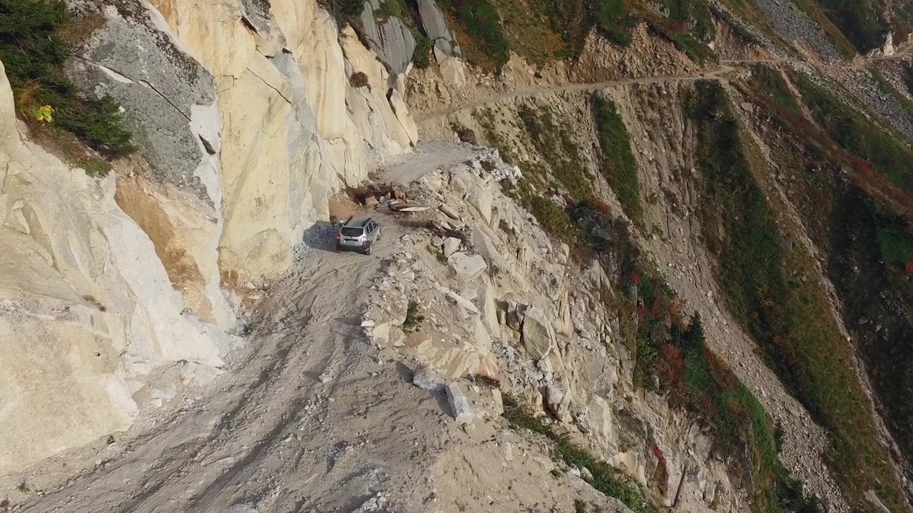 SUV argentato che percorre una stretta strada di montagna a strapiombo