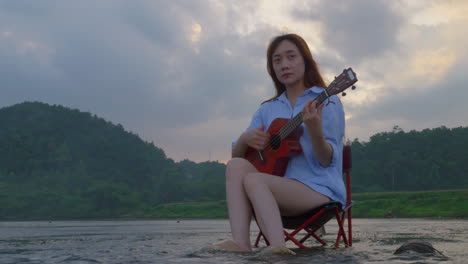 woman playing ukulele by the lake at sunset