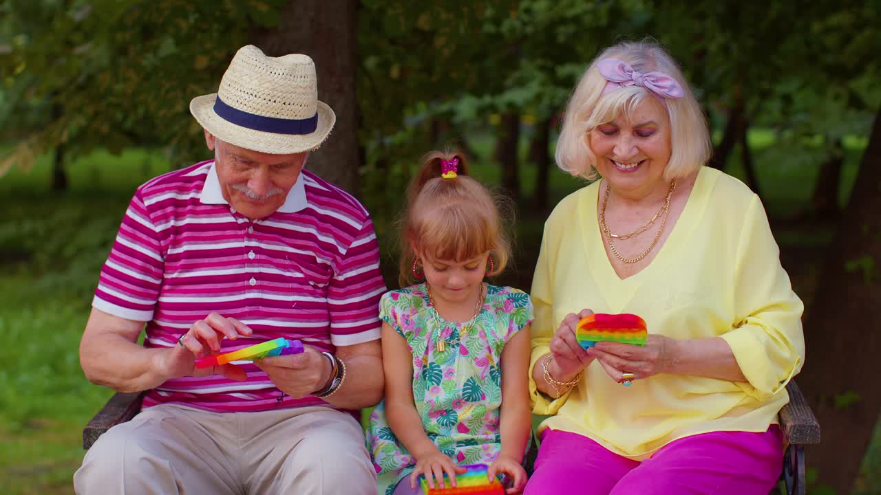 Stilvolles älteres Paar, Großeltern mit Enkelin, spielen Anti-Stress Pop-It Spiel.