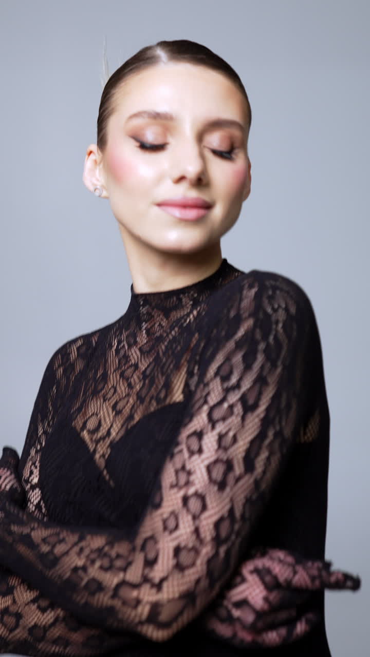 Attractive woman with professional make up wearing lace. Model raises hands and touches face posing for camera. Vertical video.