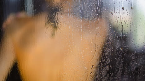 gotas de agua corren por la pared de la cabina de vidrio mujer disfruta de la ducha