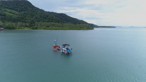 stunning aerial shot of a sinking fishing boat off the coast of a mountainous island in thailand