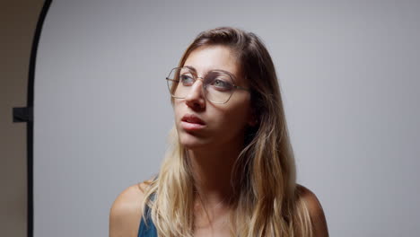 young woman in studio closes her eyes, lifts her head slightly, adjusts her hair, and turns toward the light. neutral background and soft lighting