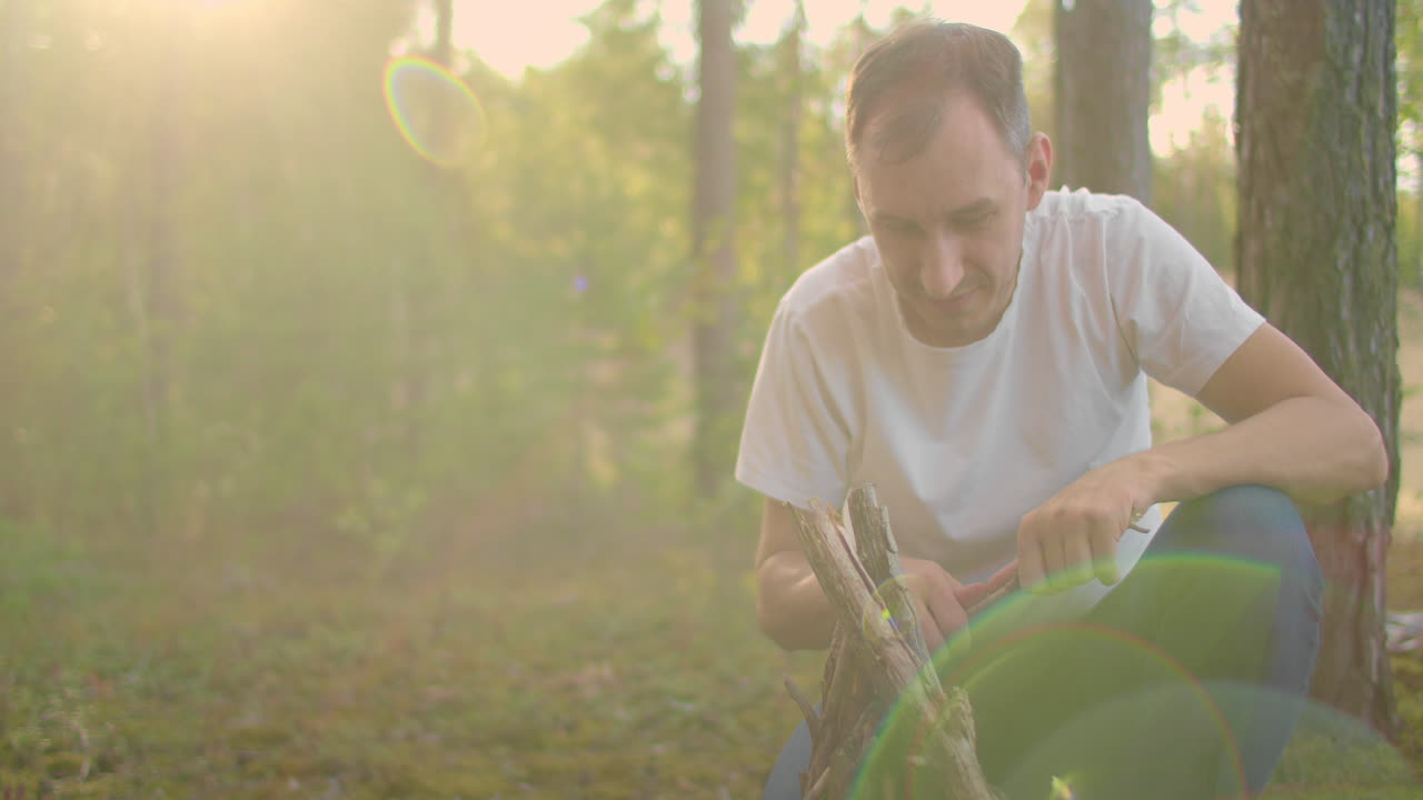 숲 속 에 있는 한 사람 이 가족 들 이 캠핑 여행 을 하는 동안 일몰 때 캠프 파이어 스틱 을 수집 하고 세우고 있다