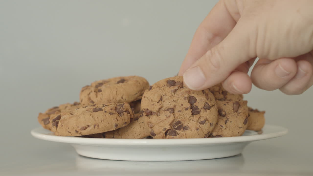 흰색 접시에 초콜릿 칩 쿠키를 손에 쥐고